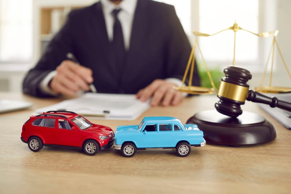 Close-up of two toy model cars in a courtroom setting with a judge conducting a lawsuit for a car accident. Toy cars symbolize the accident, placed next to the judge's gavel and the scales of justice.