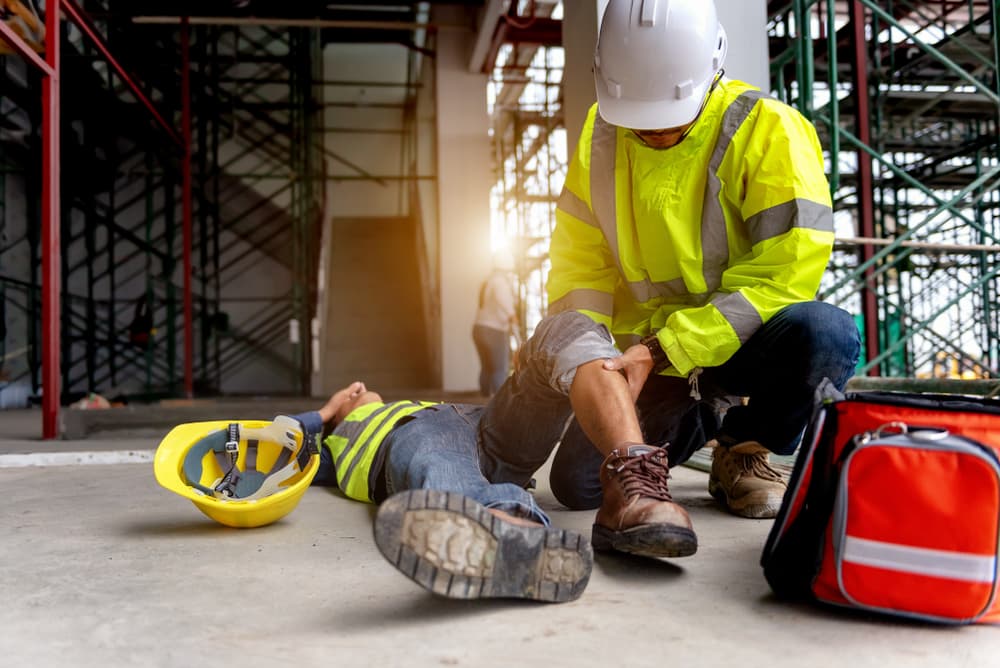 Construction worker accident at site, scaffolding falls. First aid by safety team for injured employee.