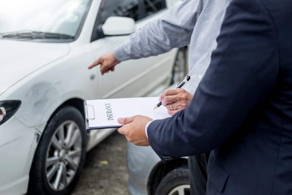 Insurance agent assesses and processes a car accident claim, documenting details on a clipboard for accurate evaluation.