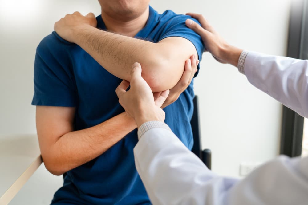 A doctor or chiropractor examining a patient for shoulder pain in a medical clinic.