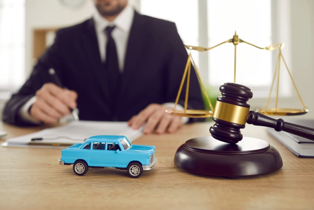 Tiny car and judge gavel symbolize legal issues in vehicle ownership. Placed on a table in front of a lawyer, signifying litigation concerns.