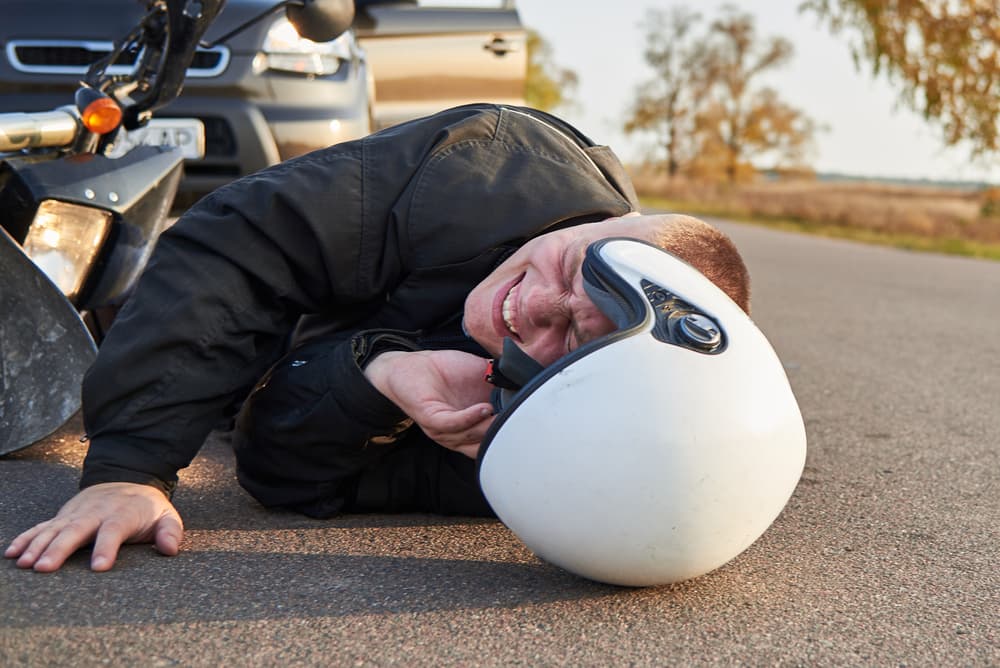 Picture showing a motorcyclist on the ground beside a motorcycle and car, illustrating the theme of road accidents.